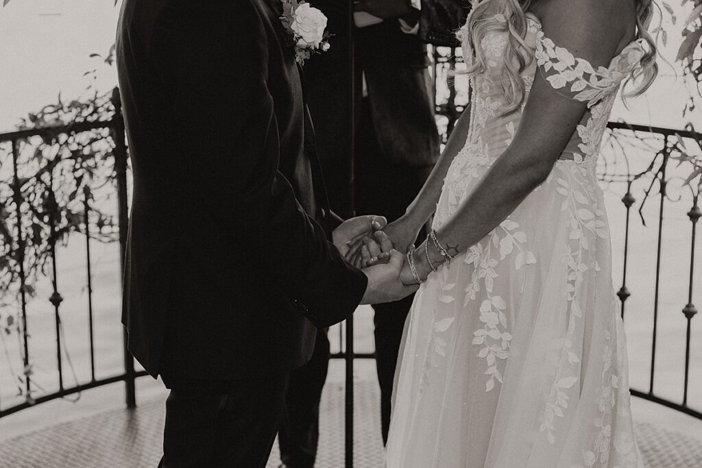 A b+w image shows newlyweds holding hands during vows at their Las Vegas elopement